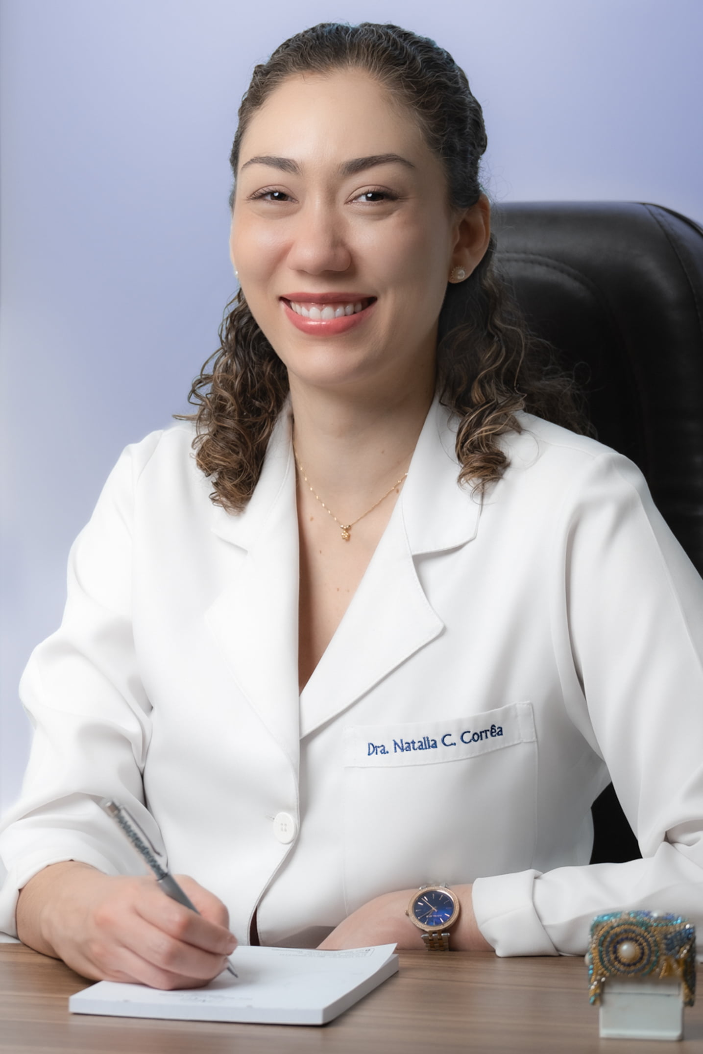 Dra. Natália Corrêa sentada na cadeira de atendimento em seu consultório.